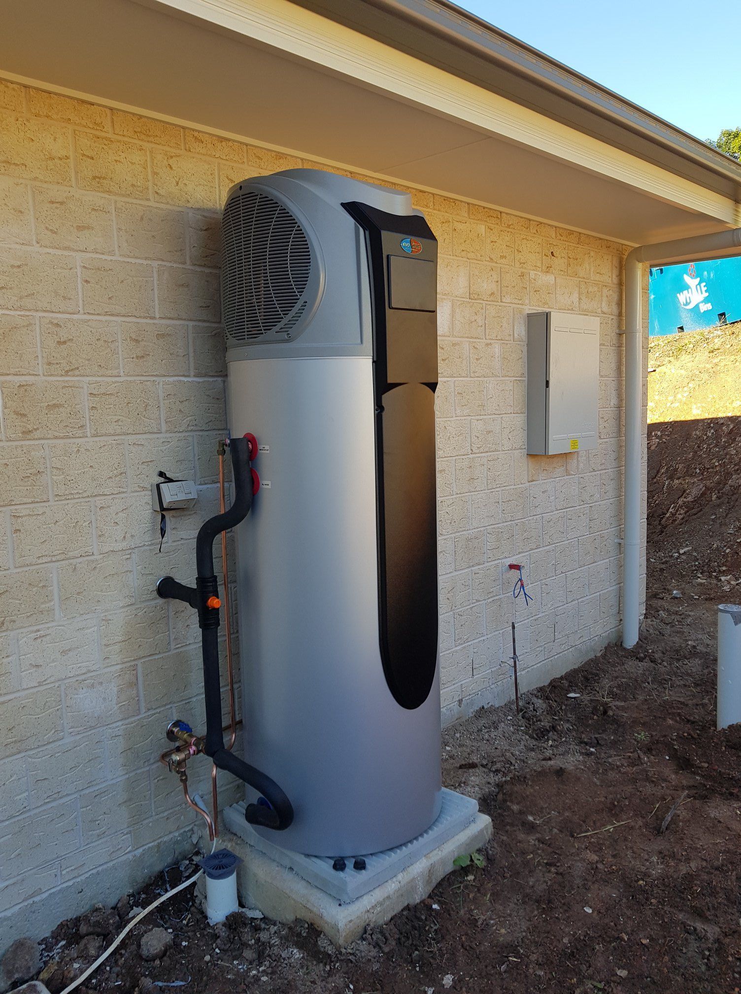 Tall Silver Heat Pump Unit Mounted on a Concrete Base, Against a Brick Wall — 24/7 Hot Water in Valdora, QLD