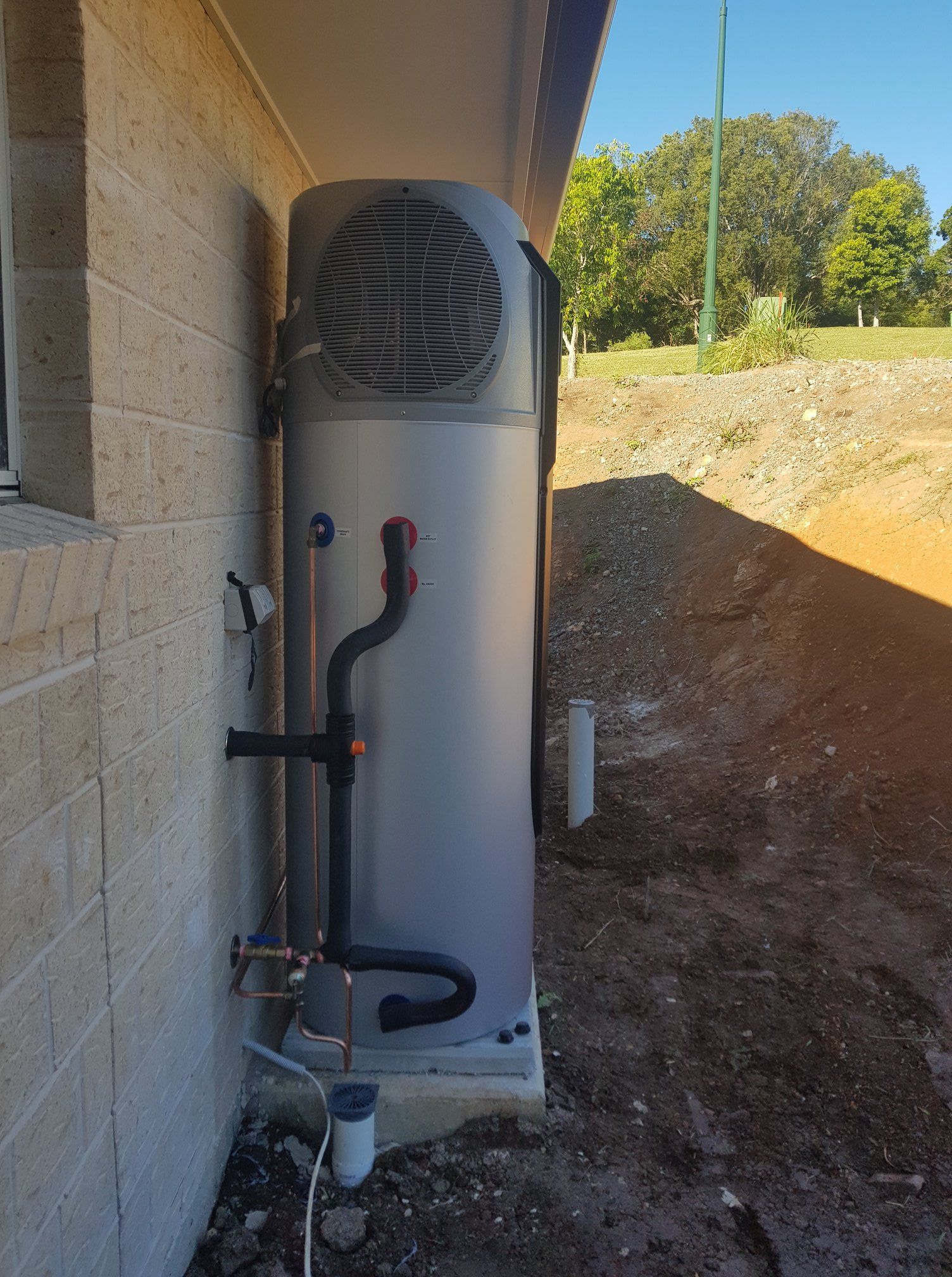 Outdoor Water Heater Next to a Brick Building; Black Pipes Attached — 24/7 Hot Water in Valdora, QLD