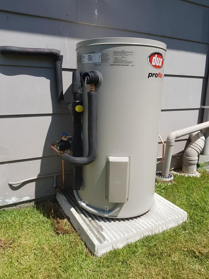 A Tall, Grey Hot Water Heater Next to a Building on a Concrete Base, Installed on Grass — 24/7 Hot Water in Valdora, QLD