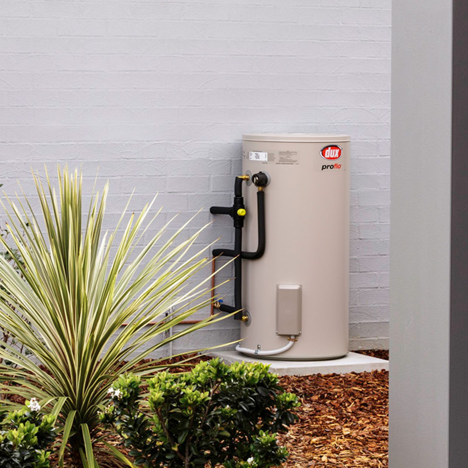 A Tall, Cylindrical Water Heater Outdoors Next to a Garden Ornament — 24/7 Hot Water in Valdora, QLD