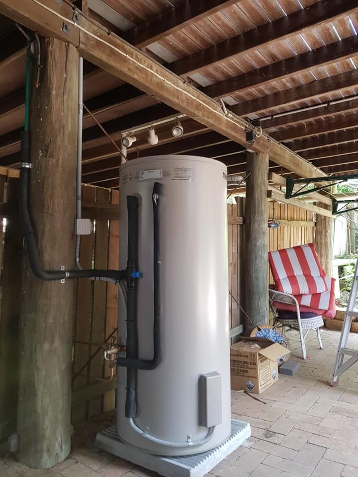 Water tank installed outdoors, under a wooden roof. Black pipes connected to the tank and running up a wooden post. — 24/7 Hot Water in Valdora, QLD