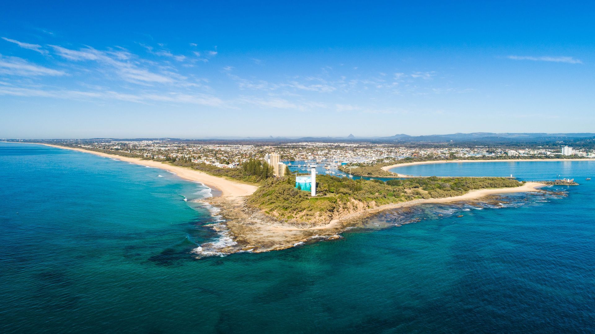 Aerial view of a coastal peninsula with a lighthouse, beach, and town under a clear blue sky — 24/7 Hot Water in Valdora, QLD