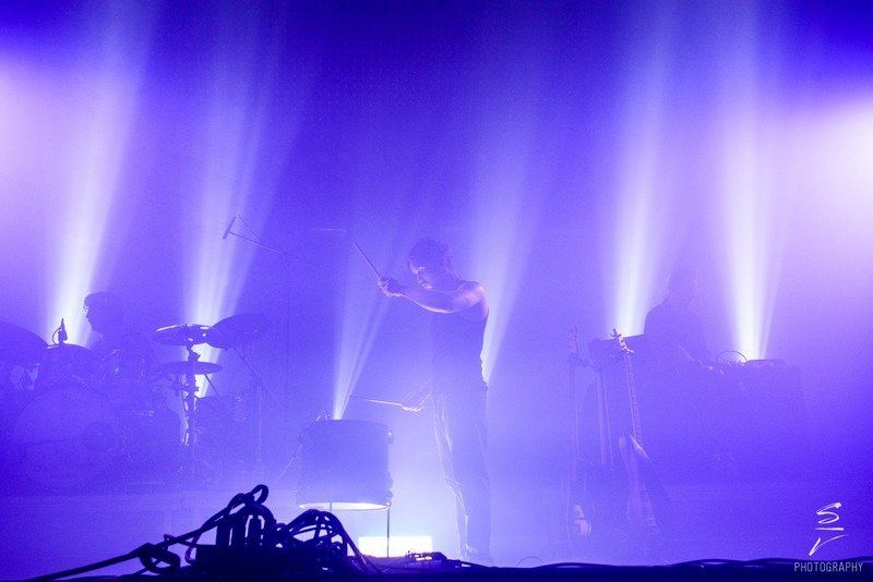 a man is standing in front of a microphone on a stage surrounded by purple lights .