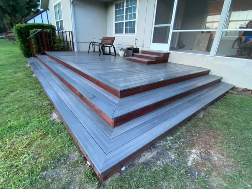 A person in work clothes and gloves uses a power drill to install wooden planks on a fence outdoors.