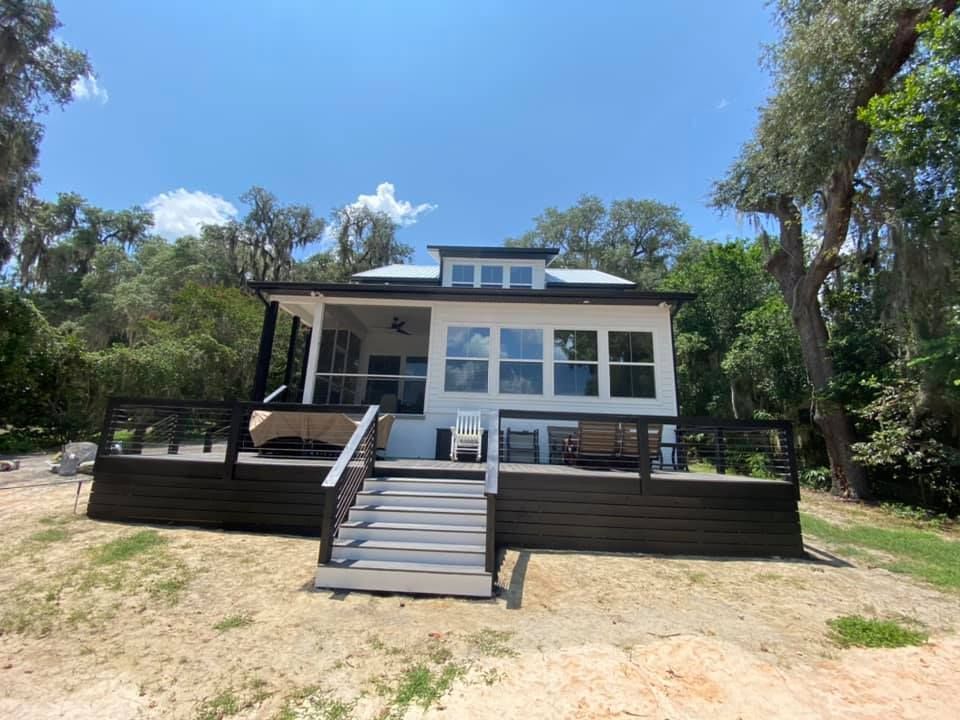 A hand using a yellow-handled brush to apply a clear finish or stain to a brown wooden picket fence.