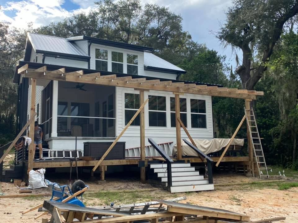 A person in a hard hat and denim shirt uses a tape measure on a countertop in a kitchen with a ladder nearby.