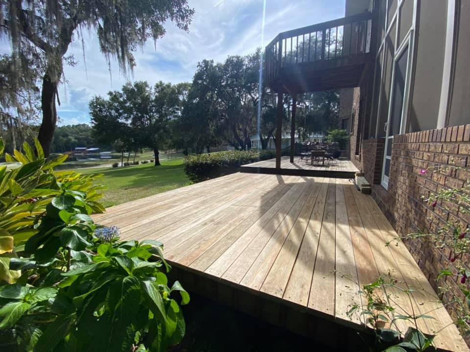A hand holds a vertical wooden fence plank steady while a power drill secures a screw into the frame.