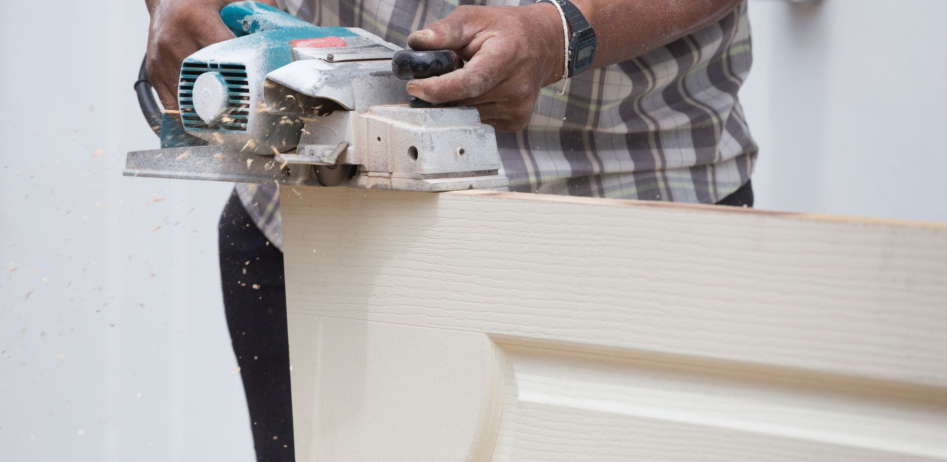 A yellow tape measure and an orange pencil resting on a rough-cut wooden board against a background of wood pieces.