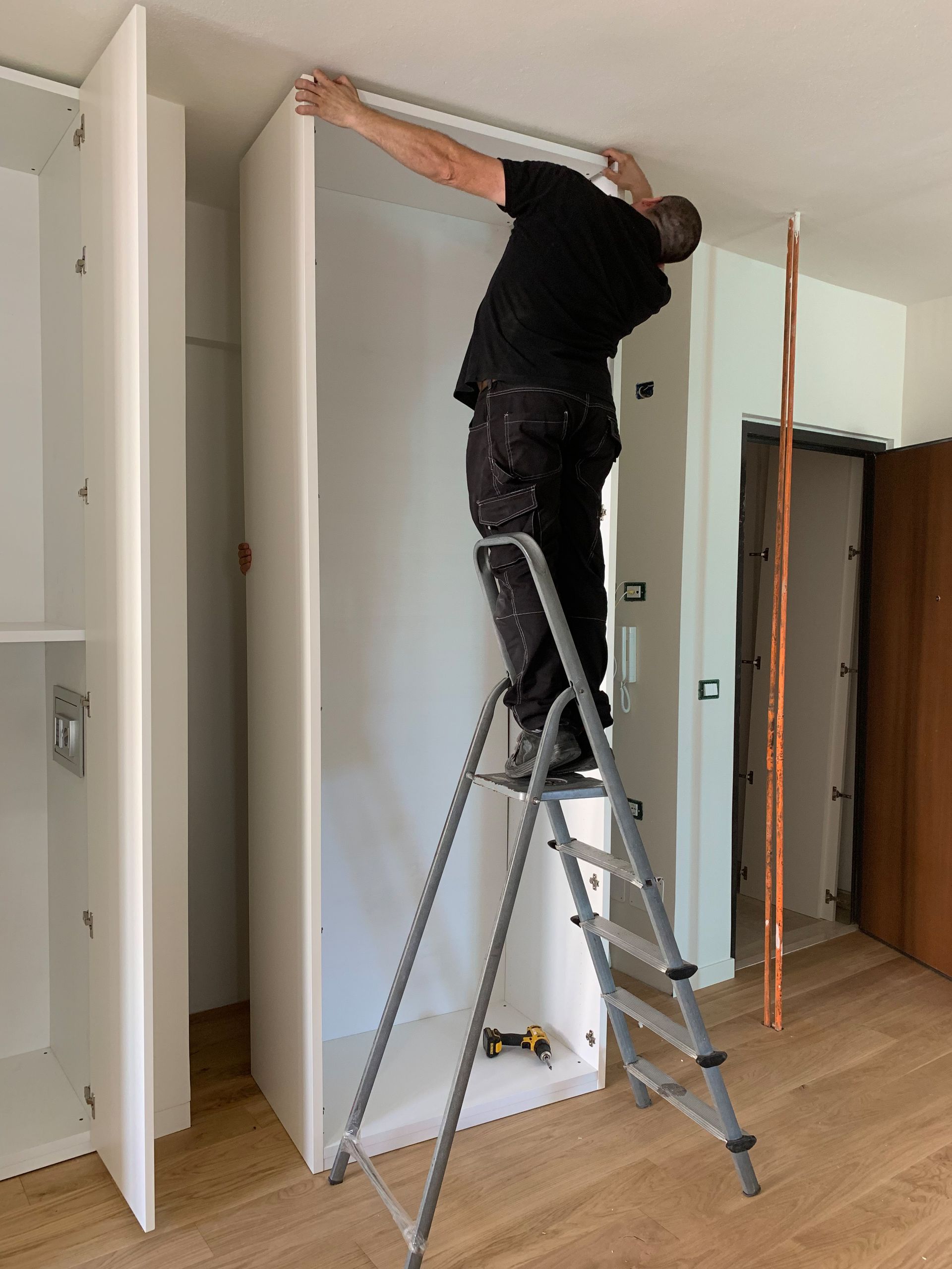 A person in work clothes installing a metal door handle onto a light wood door.