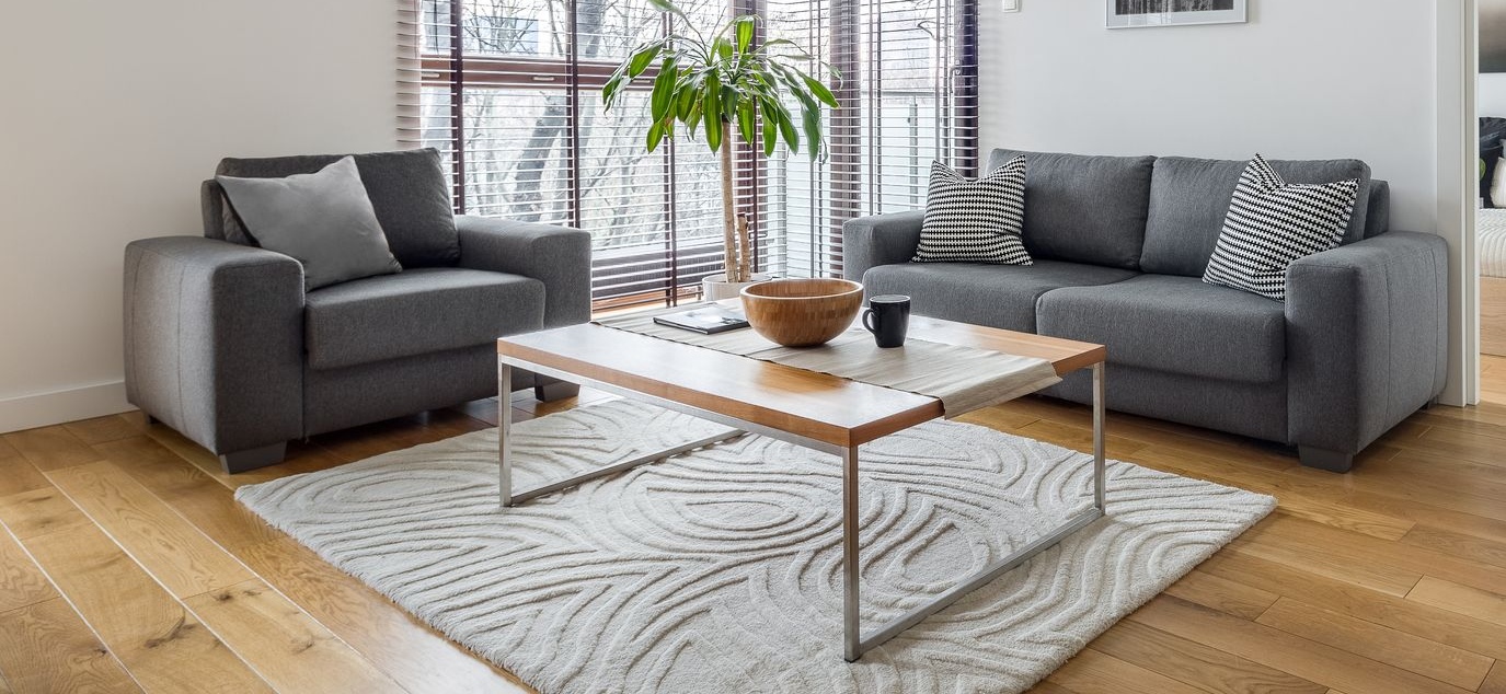 Two people kneeling on a floor, installing wooden planks with a tape measure and tool nearby.