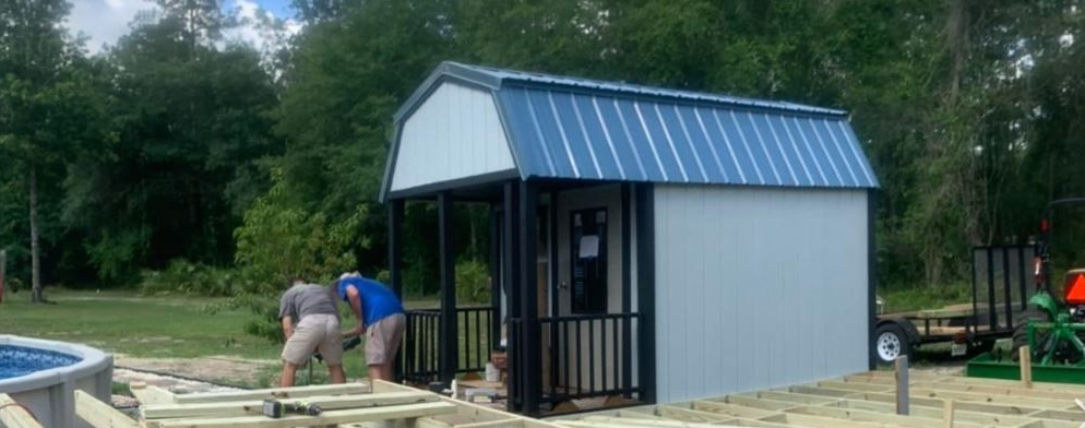 A person wearing a yellow shirt and a cap stands on a ladder, painting the exterior white wall of a house.