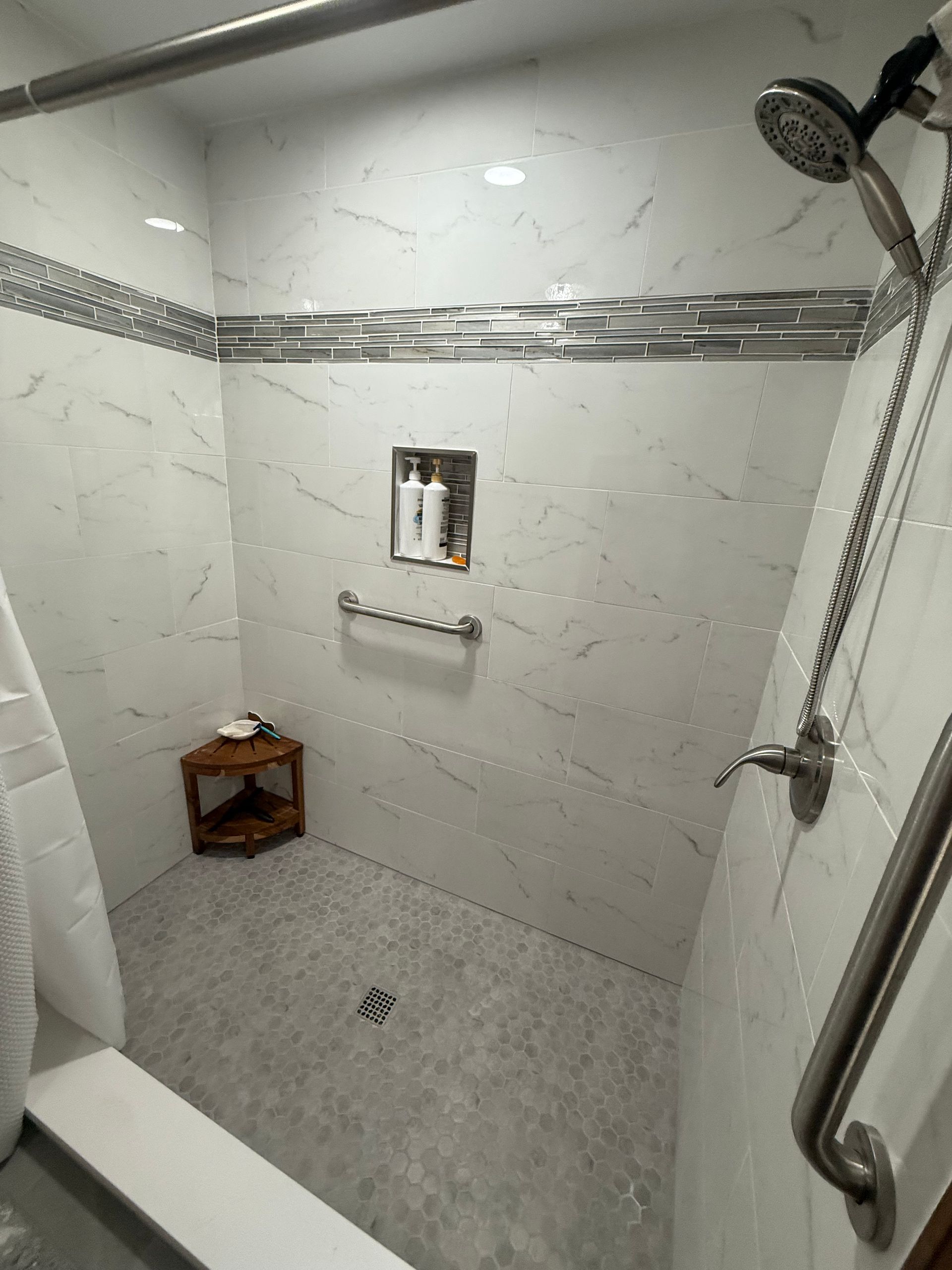 Modern bathroom featuring a white freestanding tub, marble-veined tile flooring, and a large glass-enclosed shower.
