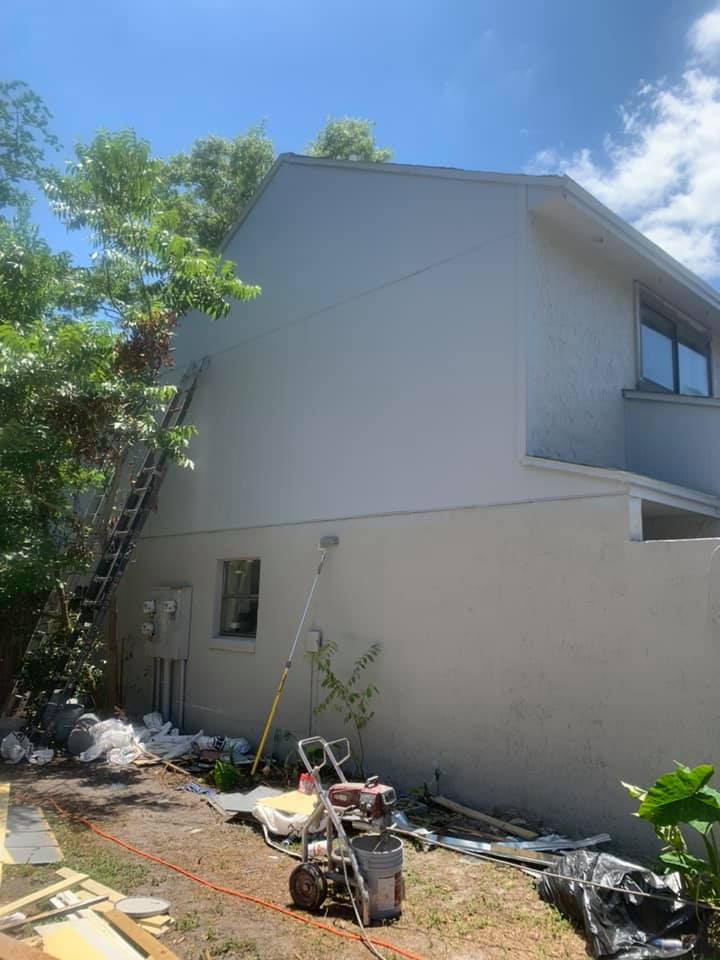 A person wearing blue work coveralls and a cap uses a paint roller to paint a white patch on a turquoise-colored wall.