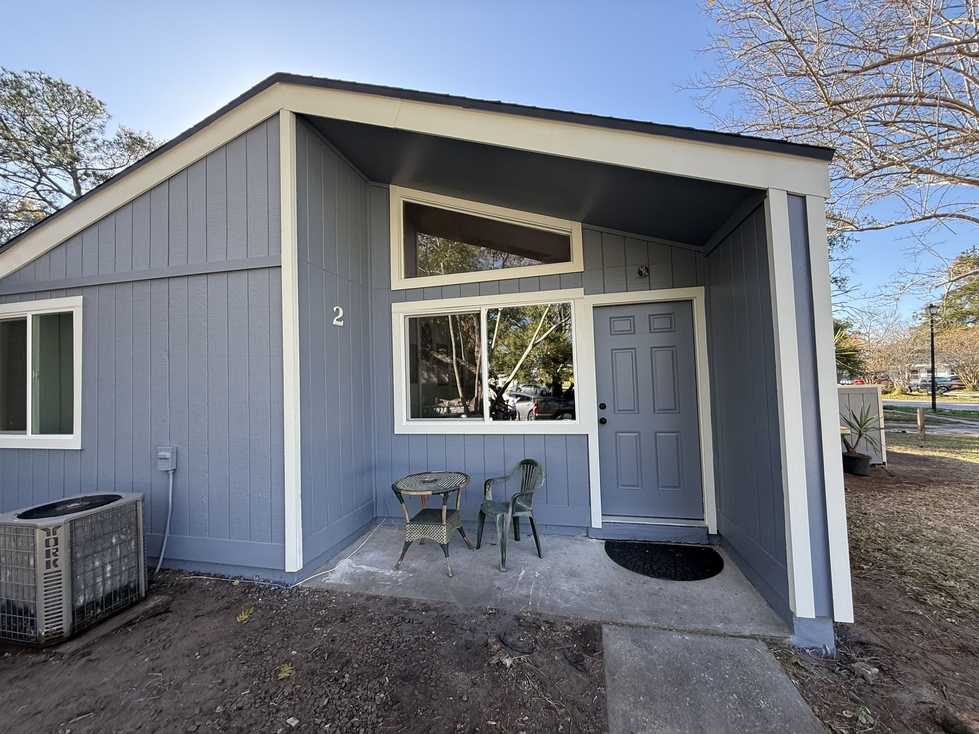 A person wearing a hard hat uses a power drill to install beige siding panels on the exterior wall of a building.