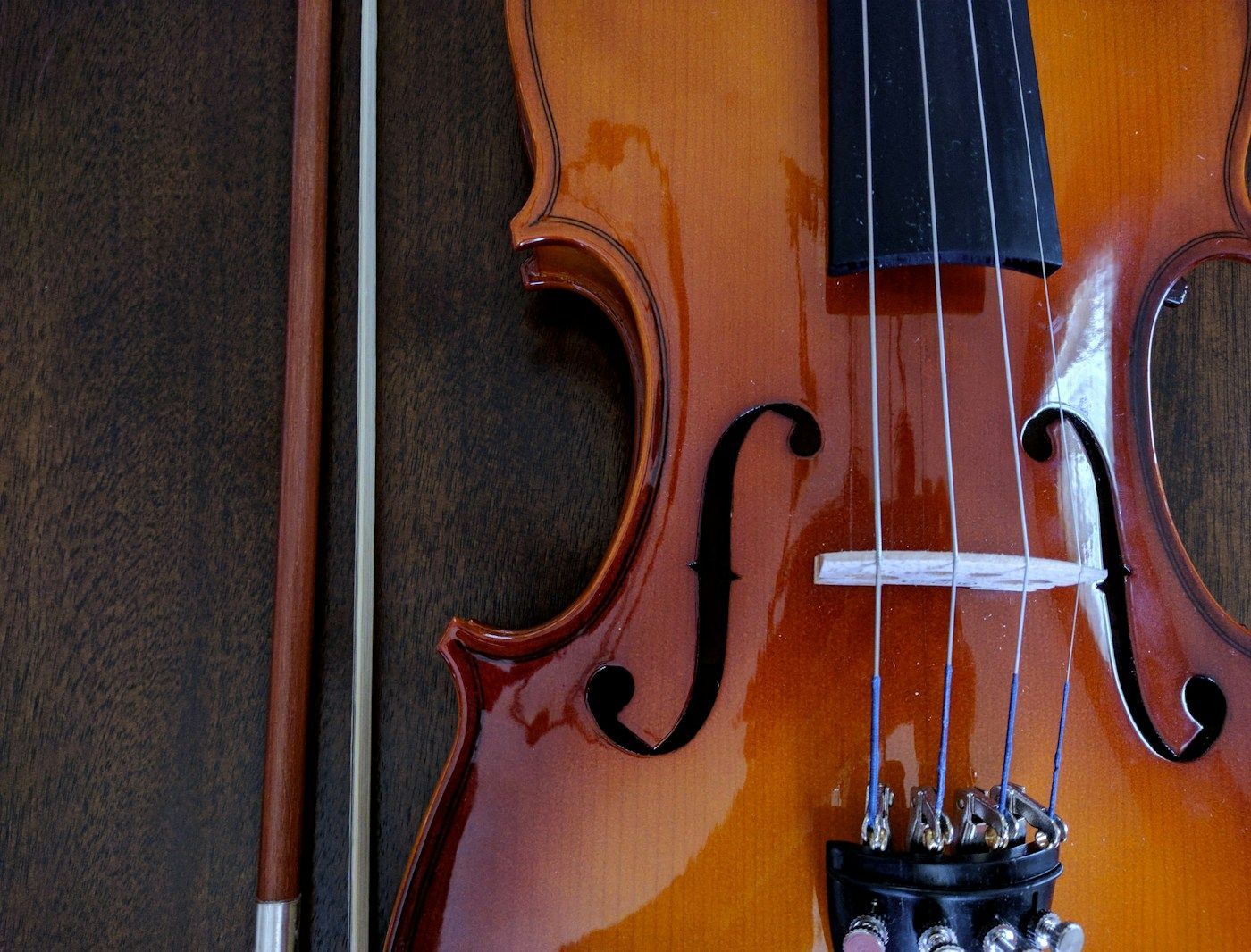 Close-up of a violin with its bow resting alongside it. The violin is wooden with dark strings.
