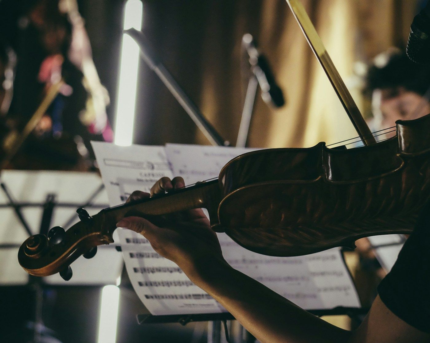 A person playing a violin with a bow, reading sheet music in an orchestra.