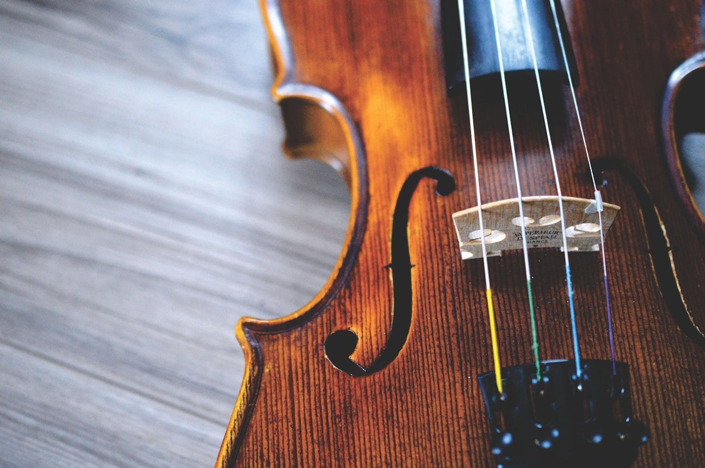 Close-up of a brown violin on a light gray wooden surface, showcasing strings and f-hole.