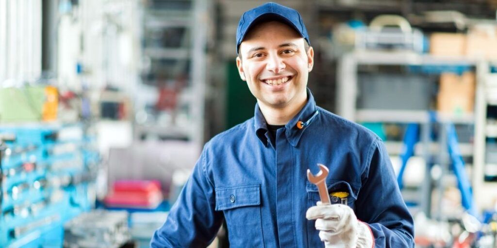 A smiling mechanic is holding a wrench in a garage. | Country Tire