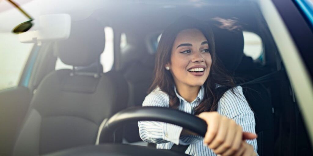 A woman is driving a car and smiling. | Country Tire