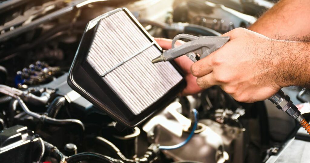 A man is holding a air filter in his hands while working on a car. | Country Tire