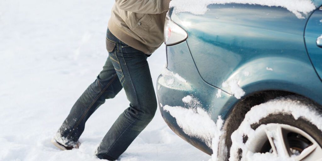 A person is pushing a car in the snow. | Country Tire