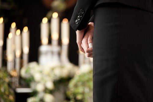 vista delle mani di un uomo in piedi con un completo nero e davanti delle candele accese