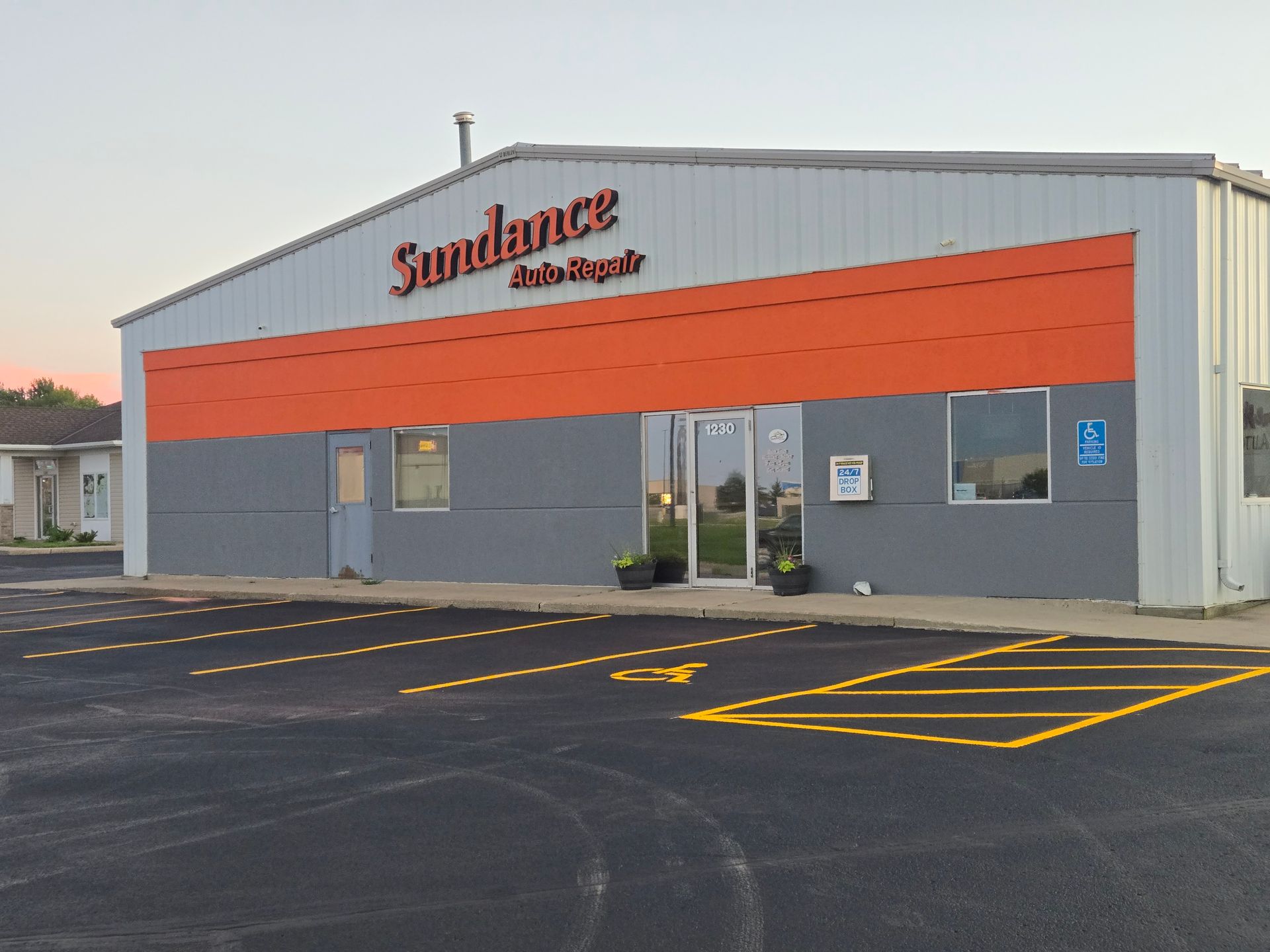 Sundance Auto Repair building with orange and gray facade, fronted by asphalt parking lot.