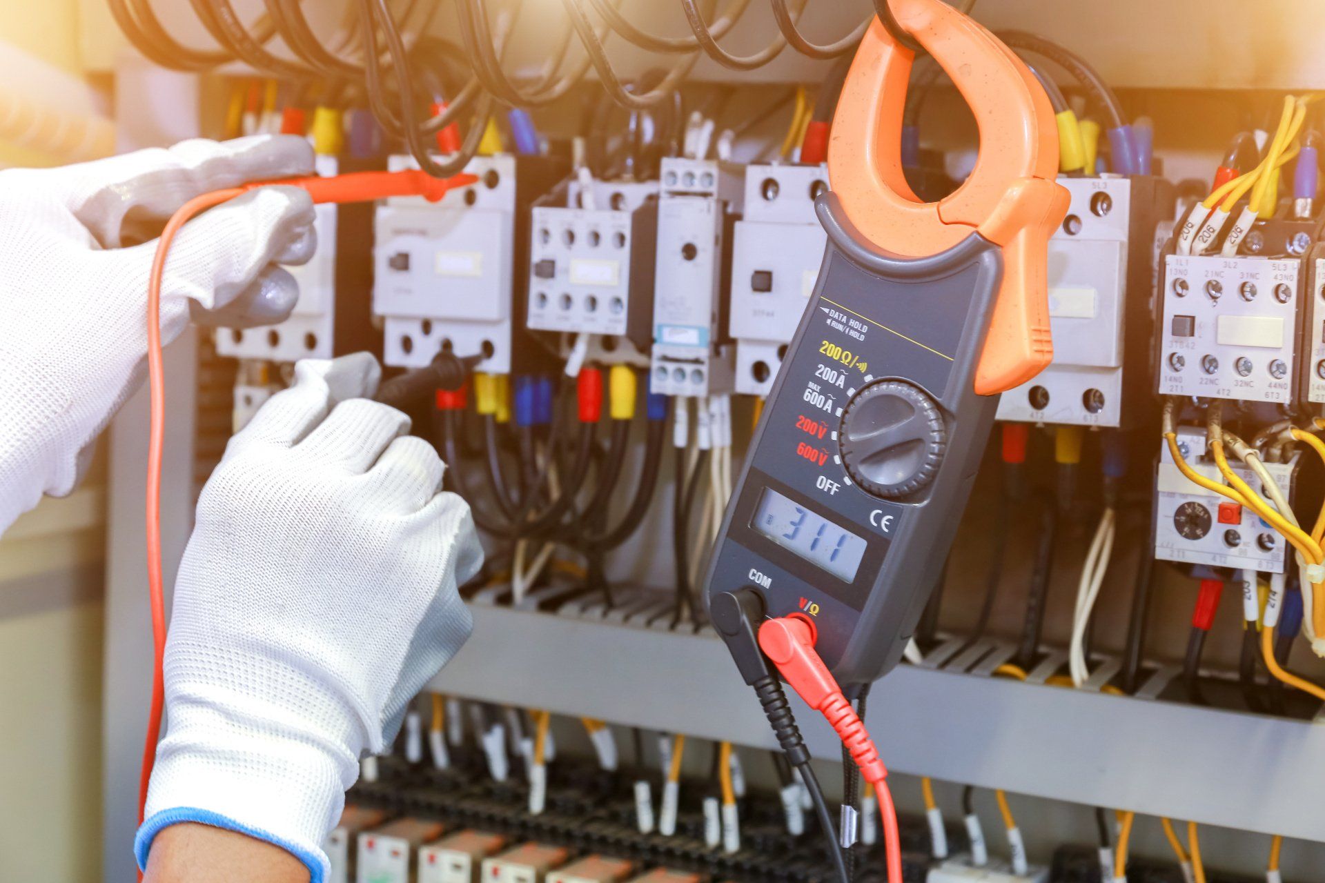 An electrician using a multimeter tester to measure electrical parameters in a control panel.