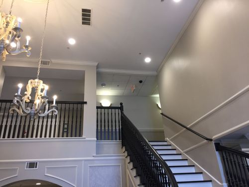 Elegant interior staircase with black railing, white walls, and chandeliers in a bright foyer