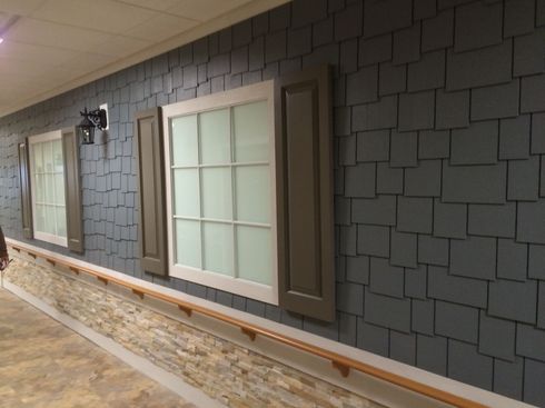 Covered outdoor walkway with gray shingle wall, white windows, and stone base trim