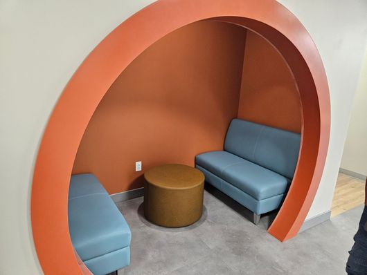 Small orange alcove seating area with blue benches and a round brown table on a gray carpet