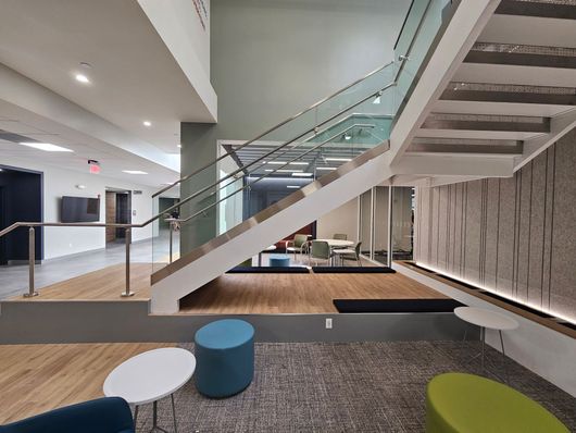 Modern lobby with stairs, glass railing, wood floor, and blue and white stools
