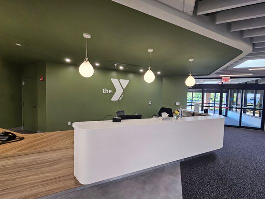 Modern lobby with white reception desk, green wall, hanging lights, and glass entrance doors
