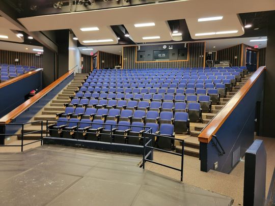 Empty lecture hall with rows of blue seats and a stage at the front