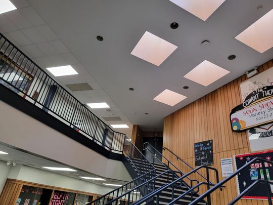 Indoor stairwell with black railings, skylights, and colorful wall signs in a bright building lobby