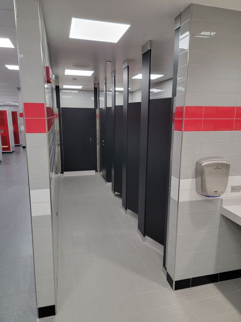 Public restroom with gray stall doors, white tiled walls, and red stripe accents.
