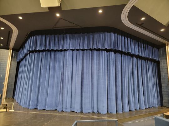 Blue stage curtain in a theater, closed across a wide curved stage entrance