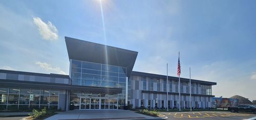 Modern glass-and-white office building with a central entrance and U.S. flag under a bright blue sky