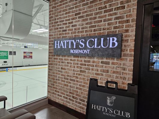 HATTY’S CLUB sign on a brick wall beside an ice rink entrance