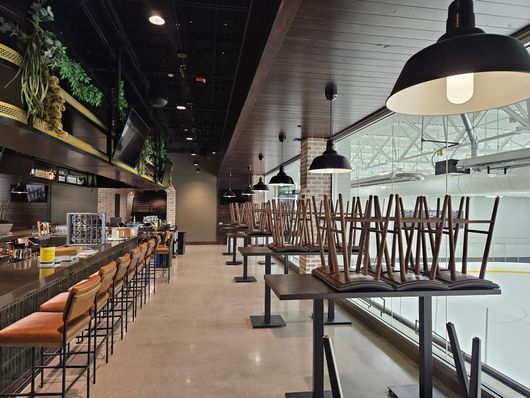 Empty modern restaurant interior with bar seating, tables, and hanging pendant lights