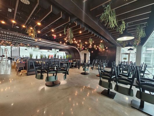 Empty restaurant interior with stacked chairs, hanging lights, and glossy floor reflections