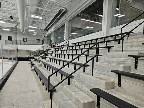 Empty indoor bleachers in a gymnasium with black railings and white seating steps