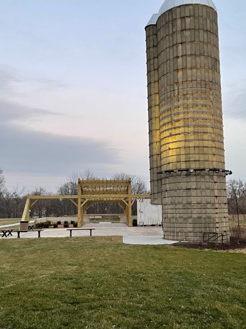 Outdoor park with a tall stone silo sculpture and a wooden bench on a grassy field at dusk
