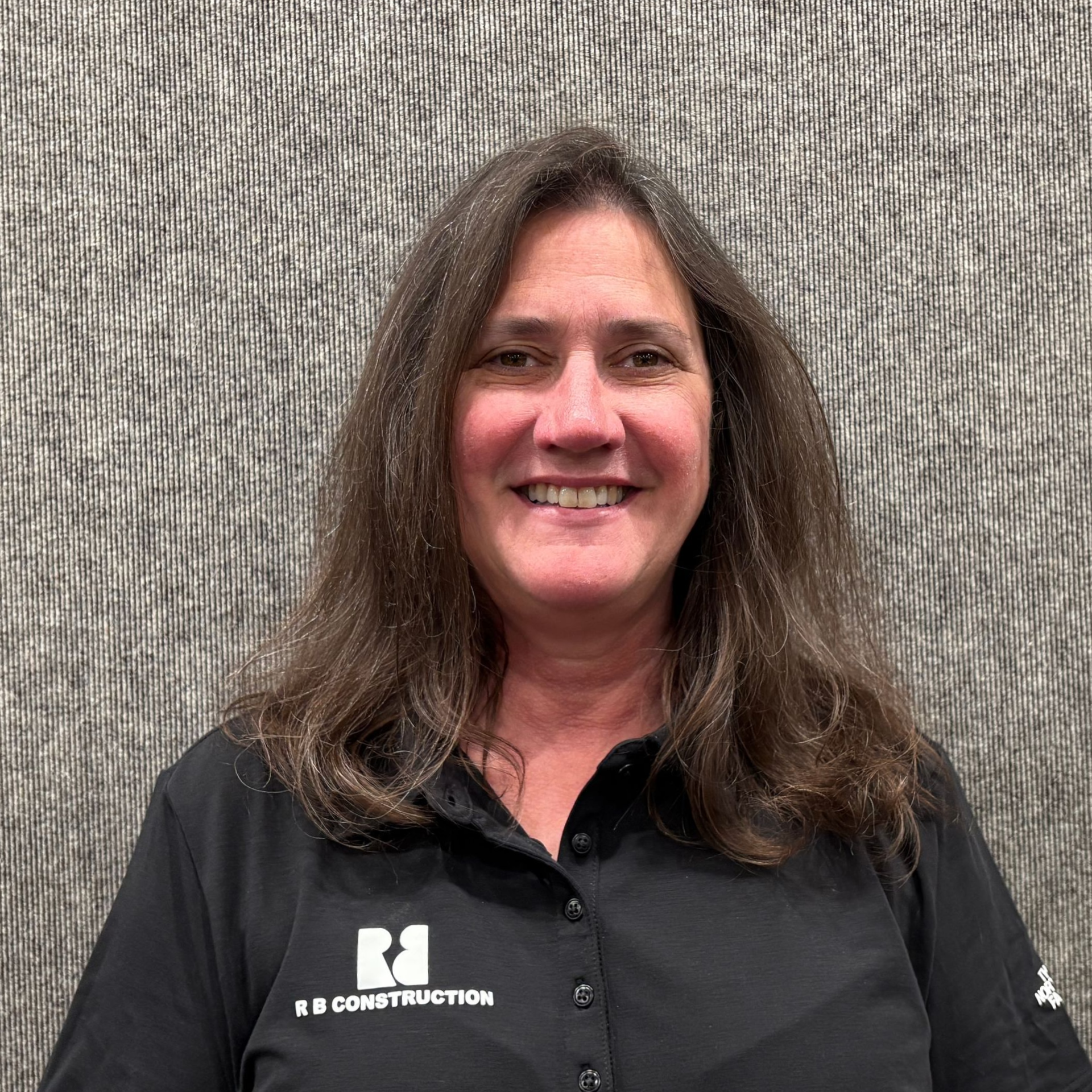 Smiling person in a black shirt standing before a textured gray wall.