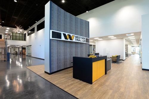 Modern office lobby with wood floors, black-and-yellow reception desk, and stairway in the background