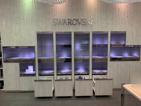 Swarovski retail display wall with illuminated glass shelves and purple-lit display cases