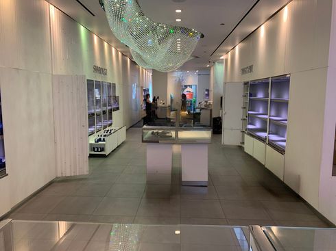 Bright modern store interior with white walls, display shelves, and a green glass chandelier.