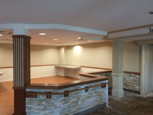 Empty indoor reception area with wood-and-stone counter, beige walls, and recessed lighting
