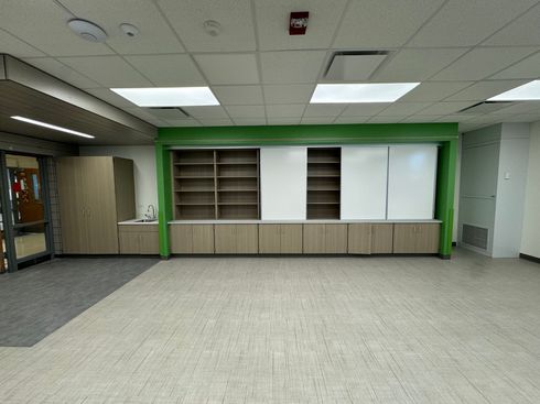 Empty office lobby with beige carpet, green accent wall, built-in cabinets, and fluorescent ceiling lights