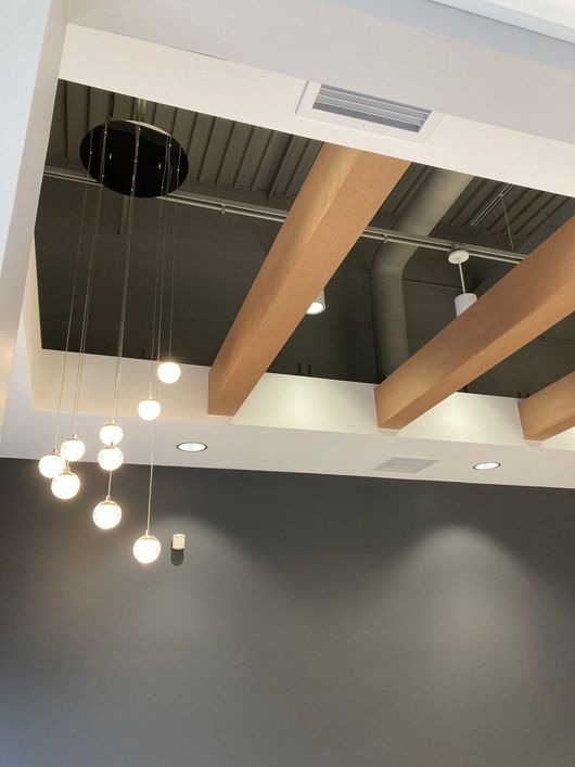 Ceiling with exposed beams and hanging pendant lights above a gray wall